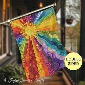 May include: A rectangular garden flag featuring a vibrant sunburst design with radiating rays in a spectrum of colors including red, orange, yellow, green, blue, and purple. The fabric displays intricate quilted textures and the text DOUBLE SIDED.