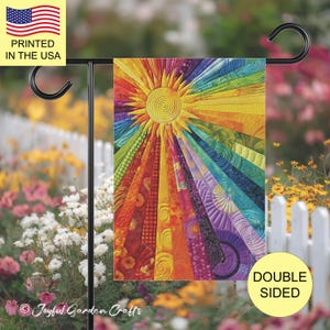 May include: A rectangular garden flag featuring a vibrant sunburst design with radiating rays in a spectrum of colors including red, orange, yellow, green, blue, and purple. The fabric displays intricate quilted textures and patterns.