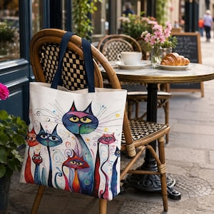 Boho cat print tote bag with navy handles hanging from a café chair beside a coffee table and flowers
