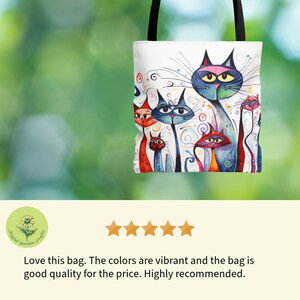 May include: White tote bag featuring a colorful illustration of stylized cats. The cats have various colors, including red, blue, and pink, with whimsical details. The bag has black handles and a green background.