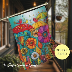 May include: Double-sided garden flag with a colourful, whimsical design. The artwork shows umbrellas, flowers, and birds against a turquoise background. The flag includes the text "Joyful Garden Crafts".