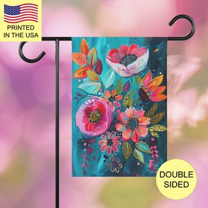 May include: A rectangular garden flag hanging on a black metal stand, featuring a vibrant floral painting with pink, red, and orange flowers against a deep teal background. The artwork displays stylized petals, leaves, and stems in a painterly style.