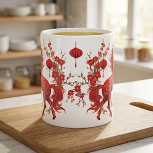 May include: A white ceramic mug with a red floral and lantern design. The mug is filled with a yellow liquid, possibly tea or coffee. The design features red flowers and lanterns, with a horse-like figure on each side.