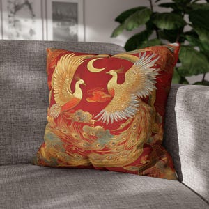Puede incluir: Cojín decorativo cuadrado con un diseño vibrante de dos fénix dorados con las alas extendidas sobre un fondo rojo. El cojín también incluye una luna creciente y detalles de nubes, lo que se suma a la estética ornamentada. Ideal para añadir un toque de elegancia.