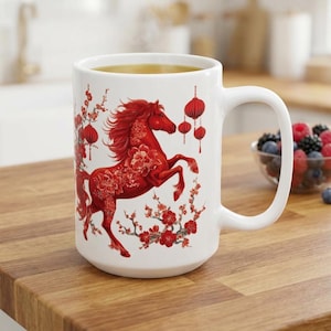 May include: White ceramic mug with a red horse design, floral and lantern details. The horse is rearing up, with floral patterns on its body. The mug has a large handle and is filled with a light-coloured liquid.