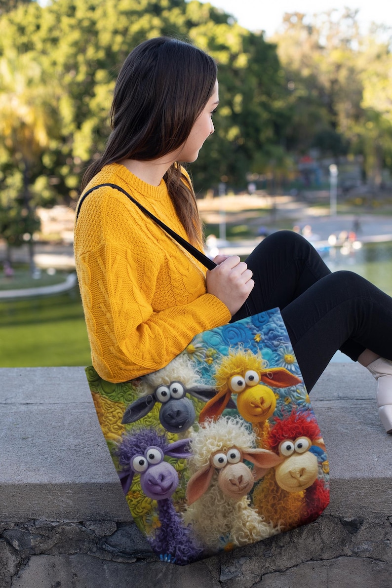 Puede incluir: Un bolso tote con una colorida ilustraci&oacute;n de ovejas de dibujos animados con lana de varios colores. El bolso tiene un fondo azul con estrellas amarillas y flores blancas. El bolso lo lleva una persona con un su&eacute;ter amarillo.
