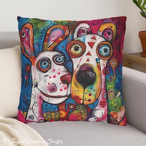 May include: Square throw pillow with a vibrant, colorful illustration of two stylized dogs. The artwork features bold lines, bright colors, and whimsical details, creating a cheerful and artistic design. The pillow is placed on a gray sofa.