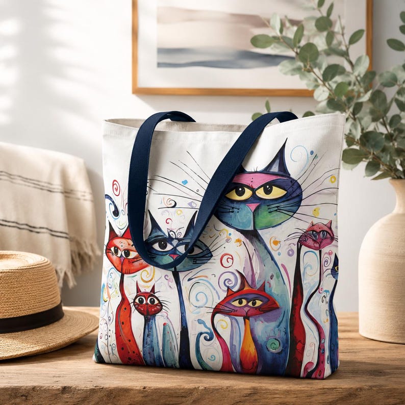 Colorful whimsical cat tote bag hanging on a café chair at an outdoor street café with coffee and pastries nearby