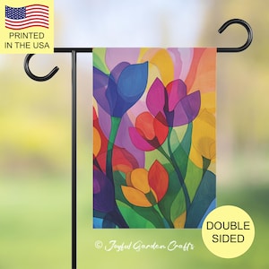 May include: Double-sided garden flag with a vibrant floral design of tulips in blue, pink, orange, and yellow. The flag is mounted on a black metal stand. Text on the flag reads "Joyful Garden Crafts" and "Printed in the USA".