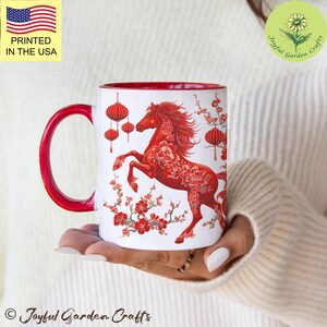 May include: White ceramic mug with a red interior and handle. The mug features a red horse design with floral accents and hanging lanterns. The text "PRINTED IN THE USA" is visible. The mug is from "Joyful Garden Crafts".