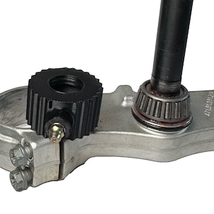 Puede incluir: Primer plano de un accesorio de carretilla elevadora de metal negro con un anillo roscado y un eje de metal plateado. El eje tiene un rodamiento y una carcasa de metal plateado.
