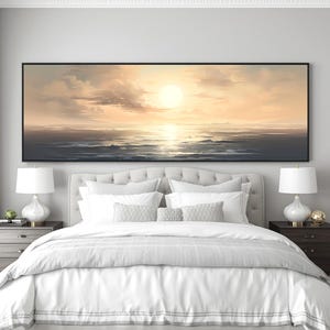 May include: A large rectangular canvas art piece depicting a sunset over the ocean. The sun is a bright yellow orb, with clouds and water in shades of gold, beige, and gray. The artwork is framed in black and hangs above a bed.