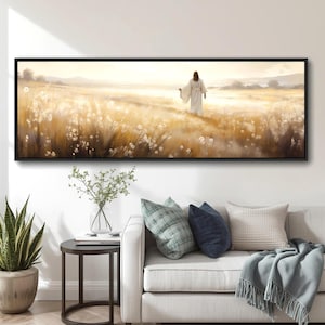 May include: A framed landscape painting shows a figure in white robes walking through a field of tall, golden grass. The artwork has a soft, ethereal quality, with a warm colour palette. The painting is displayed above a sofa with decorative cushions.