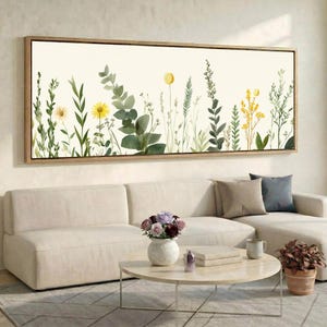 Könnte beinhalten: Ein rechteckiges Wandbild mit einer Aquarellillustration verschiedener grüner botanischer Stängel, Blätter und gelber Wildblumen auf cremefarbenem Hintergrund, eingefasst in einen dünnen, hellen Holzrahmen.