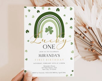 Può includere: Un invito verde e bianco con un arcobaleno e trifogli. Il testo recita "Lucky One" e "Miranda's First Birthday". L'invito è per una festa il 10 febbraio alle 14:00.