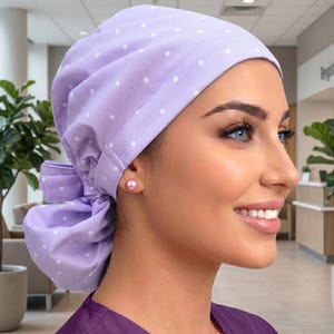 May include: A light purple scrub cap with white polka dots and a bow detail. The cap is made of soft fabric and is designed to be worn in a medical setting. The cap is a stylish and practical accessory for healthcare professionals.