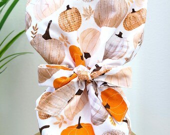 Pode incluir: Uma touca cirúrgica branca com um padrão repetido de abóboras laranja, castanhas e bege. A touca tem um laço a condizer nas costas. Design com tema de outono.