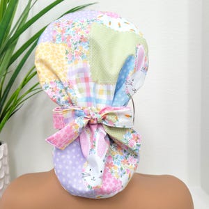 Könnte beinhalten: Eine bunte Patchwork-OP-Mütze mit Blumen- und Hasenmuster. Die Mütze ist hinten mit einer Schleife gebunden.