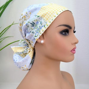 Pode incluir: Um gorro de patchwork em tons pastel. O tecido apresenta estampas florais, xadrez e botânicas em amarelo, azul e branco. O gorro é amarrado nas costas e um brinco de pérola é visível.