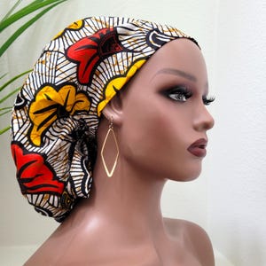 May include: A colorful bonnet with a vibrant floral pattern in red, yellow, and white. The bonnet is worn with gold diamond-shaped earrings. The fabric has a black background with a repeating design.