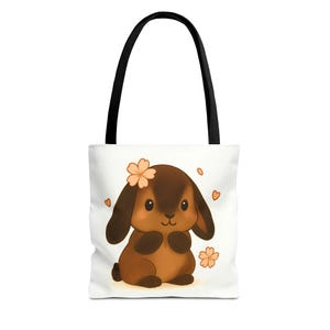 Könnte beinhalten: Weiße Tragetasche mit einer Cartoon-Hasen-Illustration. Der Hase ist braun mit langen Ohren und einer Blume. Das Design umfasst orangefarbene Herzen und Blumen. Die Tasche hat schwarze Griffe.