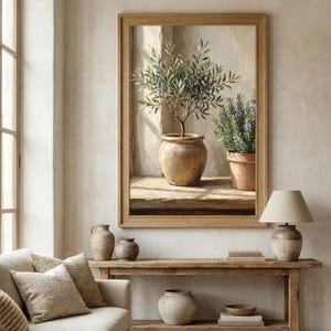 May include: A framed painting depicts an olive tree in a terracotta pot, next to a rosemary plant in a similar pot. The artwork is set in a sunlit window, with a neutral color palette. The painting is displayed above a wooden console table.