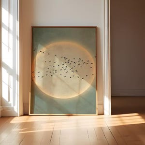 May include: A framed art print featuring a flock of black birds in flight against a soft, glowing circular background. The artwork has a muted color palette with a light green and tan color scheme. The frame is a warm brown color.
