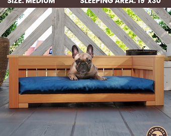 May include: A medium wooden patio sofa for pets with a blue cushion. The sleeping area is 48cm x 76cm. A French Bulldog is lying on the cushion. The sofa is made of light-colored wood and has a modern design.