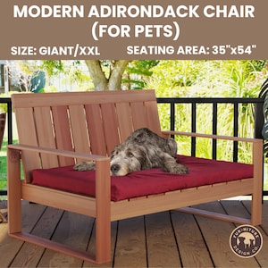 May include: A large, wooden Adirondack chair designed for pets. The chair is made of natural wood and has a red cushion. A grey dog is lying on the cushion. The chair is labeled "Modern Adirondack Chair (For Pets)" and "Size: Giant/XXL" and "Seating Area: 35"x54"". The chair is on a wooden deck.