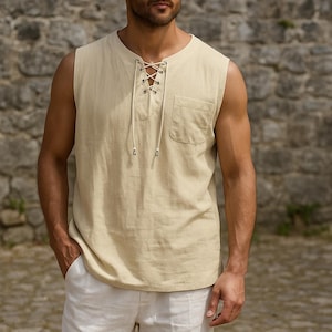 May include: A sleeveless, beige linen shirt with a lace-up neckline and a single pocket. The shirt is paired with white linen pants. The outfit is casual and suitable for warm weather.