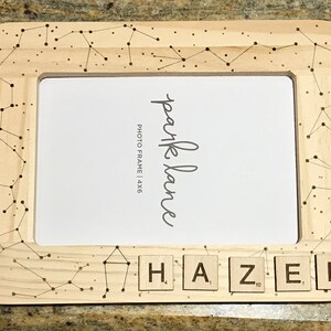 May include: A wooden photo frame with a constellation design and the word "Hazel" spelled out with letter tiles. The frame is 4x6 inches.