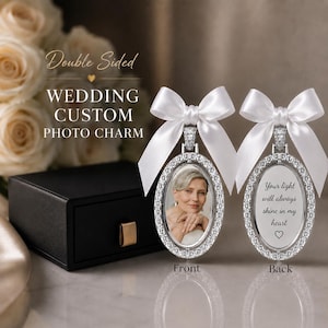 May include: A double-sided oval photo charm featuring a silver-toned frame with embedded crystals and a white satin ribbon bow. One side displays a portrait of a person, while the other side features the text: Your light will always shine in my heart.