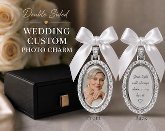 May include: A double-sided oval photo charm featuring a silver-toned frame with embedded crystals and a white satin ribbon bow. One side displays a portrait of a person, while the other side features the text: Your light will always shine in my heart.