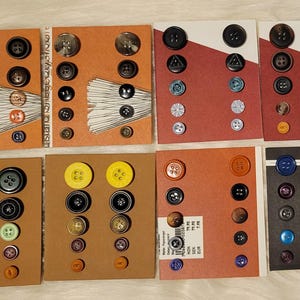 Op de afbeelding: Een assortiment van kleurrijke knopen in verschillende vormen en maten, gepresenteerd op tien kaarten. De knopen zijn gerangschikt in rijen en kolommen, waarbij sommige kaarten een zwarte achtergrond hebben en andere een bruine achtergrond.