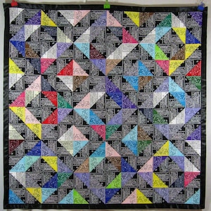 May include: A quilt made of colorful bandanas sewn together in a geometric pattern. The quilt is black with a variety of colors including red, blue, green, yellow, and purple. The bandanas are arranged in a repeating pattern of triangles.