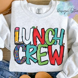 Może przedstawiać: Szara bluza z napisem "Lunch Crew" w kolorowych, kresk&oacute;wkowych literach. Litery są ozdobione wzorami w szkolnym stylu, takimi jak oł&oacute;wki, jabłka i klocki alfabetu.