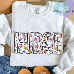 Puede incluir: Una sudadera gris claro con la palabra "NURSE" en letras grandes y delineadas. Las letras están rellenas con un patrón de calabazas, fantasmas, telarañas y calaveras en naranja, rosa y blanco, ideal para Halloween.