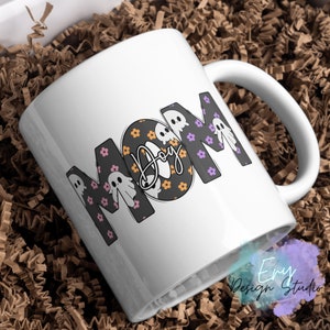 Pode incluir: Caneca de caf&eacute; de cer&acirc;mica branca com um design em preto e branco que diz "MOM" com fantasmas e flores. A palavra "Boo" est&aacute; escrita em it&aacute;lico dentro do "O".