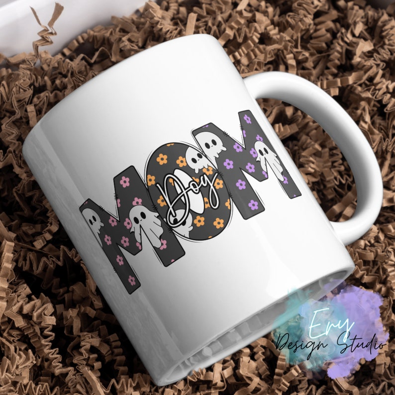 Pode incluir: Caneca de caf&eacute; de cer&acirc;mica branca com um design em preto e branco que diz "MOM" com fantasmas e flores. A palavra "Boo" est&aacute; escrita em it&aacute;lico dentro do "O".