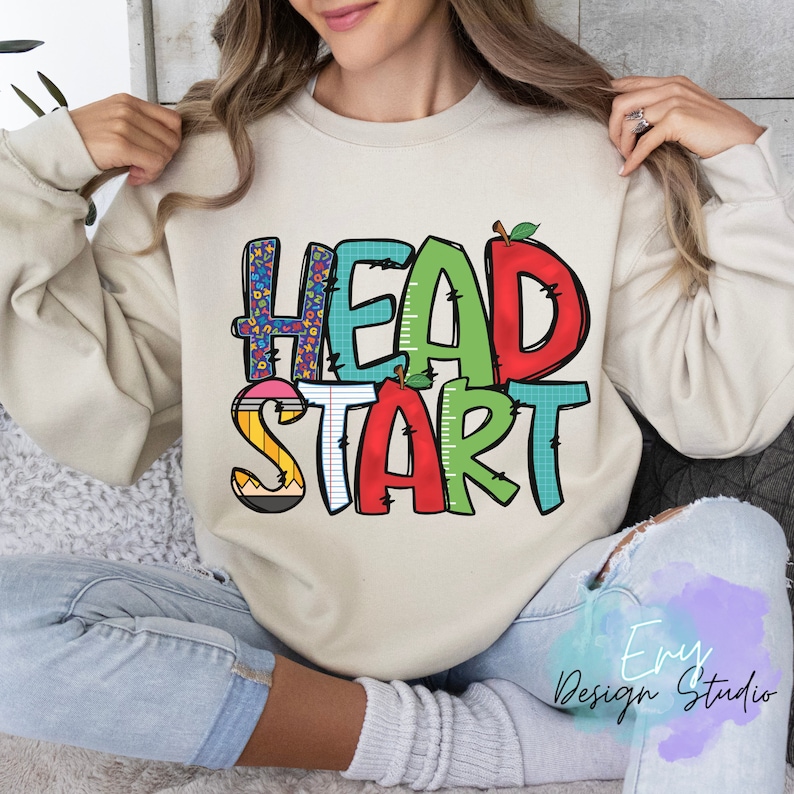 May include: A beige sweatshirt with the words "HEAD START" in colorful, playful letters. The letters are decorated with school-themed patterns like pencils, rulers, and alphabet blocks.