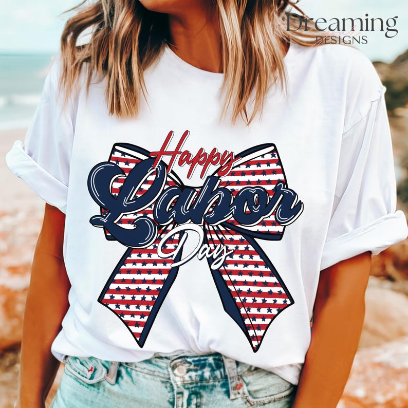 Puede incluir: Camiseta blanca con un gran gráfico de un lazo patriótico. El lazo presenta rayas rojas y blancas con estrellas azules, y las palabras "Happy Labor Day" en escritura roja y azul.