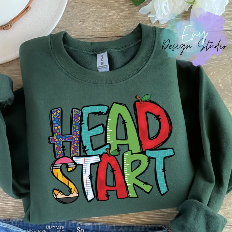 May include: A dark green sweatshirt with the words "HEAD START" printed on the front in colorful, playful letters. The letters are decorated with school-themed patterns like pencils, rulers, and apples.