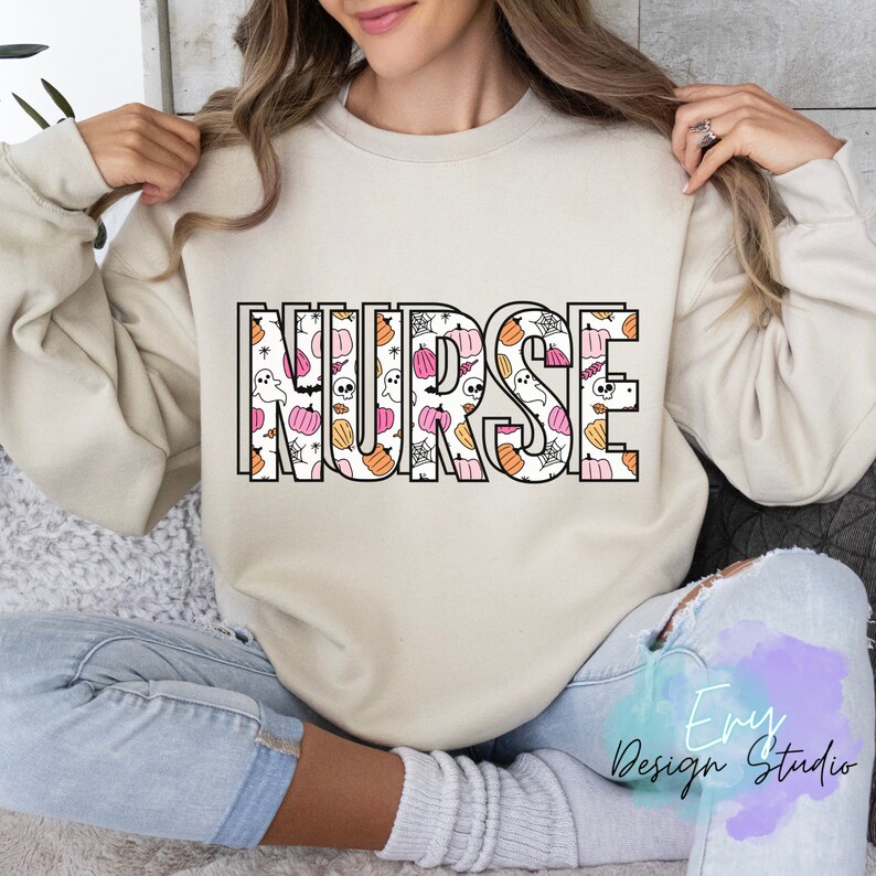 Puede incluir: Sudadera beige con la palabra "NURSE" en letras grandes y contorneadas. Las letras est&aacute;n rellenas con un patr&oacute;n de calabazas rosas y naranjas, fantasmas y telara&ntilde;as, ideal para Halloween. La sudadera es de estilo casual y c&oacute;modo.