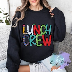 Może przedstawiać: Czarna bluza z napisem "Lunch Crew" w kolorowych literach z motywem szkolnym. Litery są ozdobione obrazkami oł&oacute;wk&oacute;w, jabłek i papieru w kratkę.