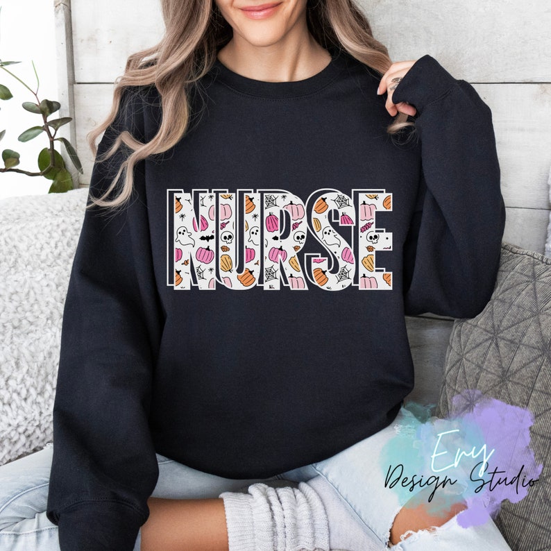 Puede incluir: Sudadera negra con la palabra "NURSE" en letras grandes con contorno blanco. Las letras est&aacute;n rellenas con un patr&oacute;n de calabazas, fantasmas y telara&ntilde;as en naranja, rosa y blanco. Un dise&ntilde;o tem&aacute;tico de Halloween.