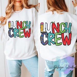 Może przedstawiać: Biała bluza z napisem "Lunch Crew" w kolorowych literach z motywem szkolnych artykuł&oacute;w. Litery są obwiedzione czarną ramką i wypełnione r&oacute;żnymi kolorami i wzorami.