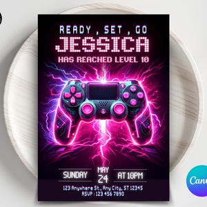 May include: A pink and blue gamer-themed birthday invitation with the text "READY, SET, GO JESSICA HAS REACHED LEVEL 10". The invitation features a pink and blue video game controller with lightning bolts in the background. The date and time of the party are listed as "SUNDAY MAY 24 AT 10PM".