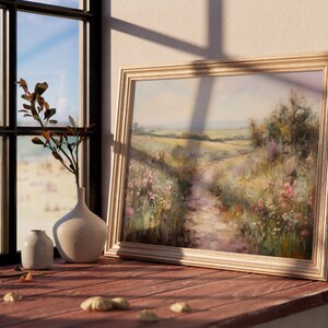 May include: A framed painting of a rural landscape with a dirt path leading through a field of wildflowers. The painting is in a light wood frame and is hanging on a wall.
