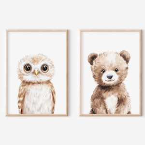 May include: Two framed watercolor prints featuring adorable woodland creatures. One print showcases a wide-eyed owl with brown and white feathers. The other print depicts a cute brown bear with a white chest and a sweet expression. Both are framed in light wood.