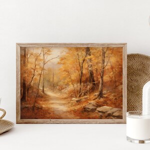 May include: A framed painting of a forest path in autumn. The trees are a mix of yellow, orange, and brown, and the path is lined with fallen leaves. The painting is set against a white background.